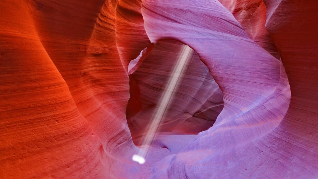 A stunning view of Antelope Canyon with its smooth, wavy walls in shades of red and purple, and a beam of light piercing through the narrow canyon.