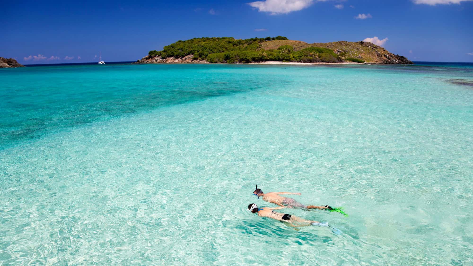 Two snorkelers explore the shallow, turquoise waters near a small island.