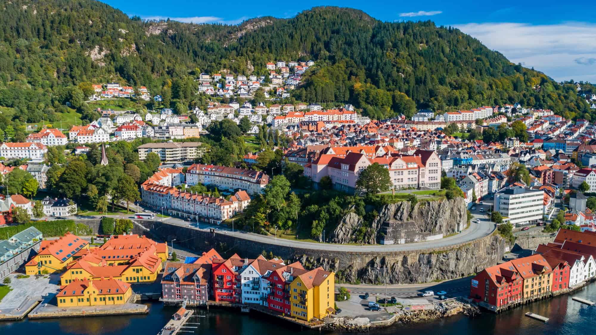An aerial view of Bergen, Norway where you can see the colored houses along the coast along with the downtown area and mountains behind