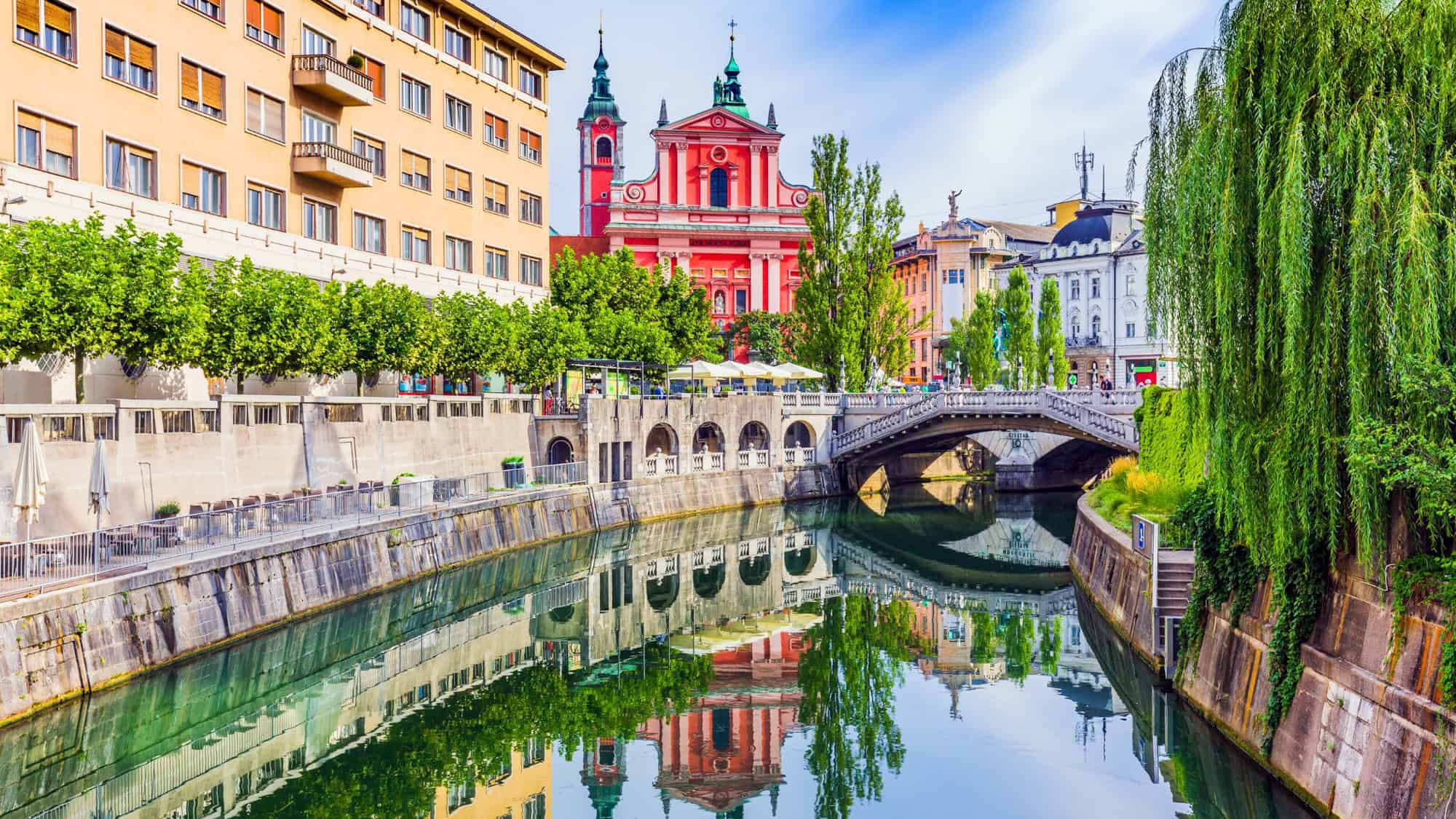 Ljubljana canal with beautiful buildings in reds and colors along with large green trees.
