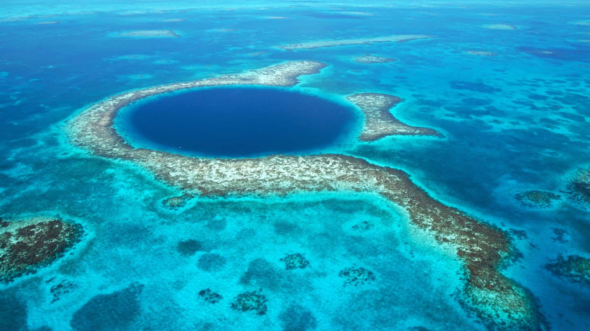 The blue hole at the Belize Barrier Reef is a dark water deep hole in the midst of shallower turquoise water.