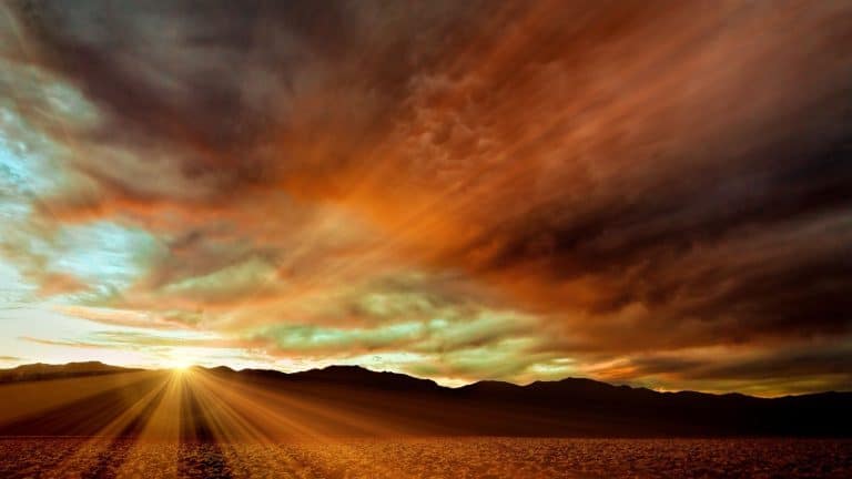 Sunset in death valley creates a sun burst as the sun creeps below the edge of the distance mountains under a pink sky.