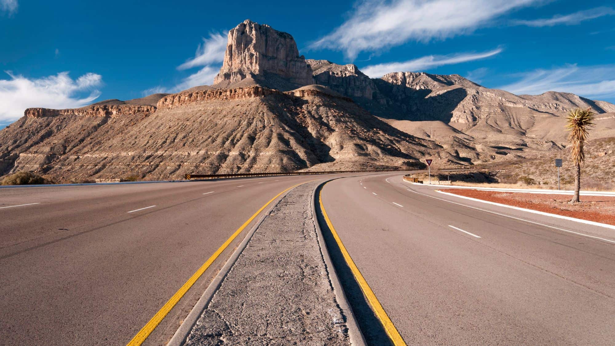 Guadalupe Mountains stand tall and proud running along the roadway under a blue sky.