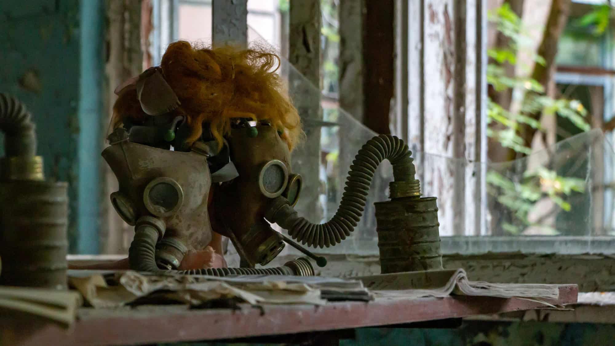 Two old, dusty gas masks with curly hair attached, resting on a windowsill in an abandoned building. The scene is filled with a sense of desolation and remnants of a bygone era.