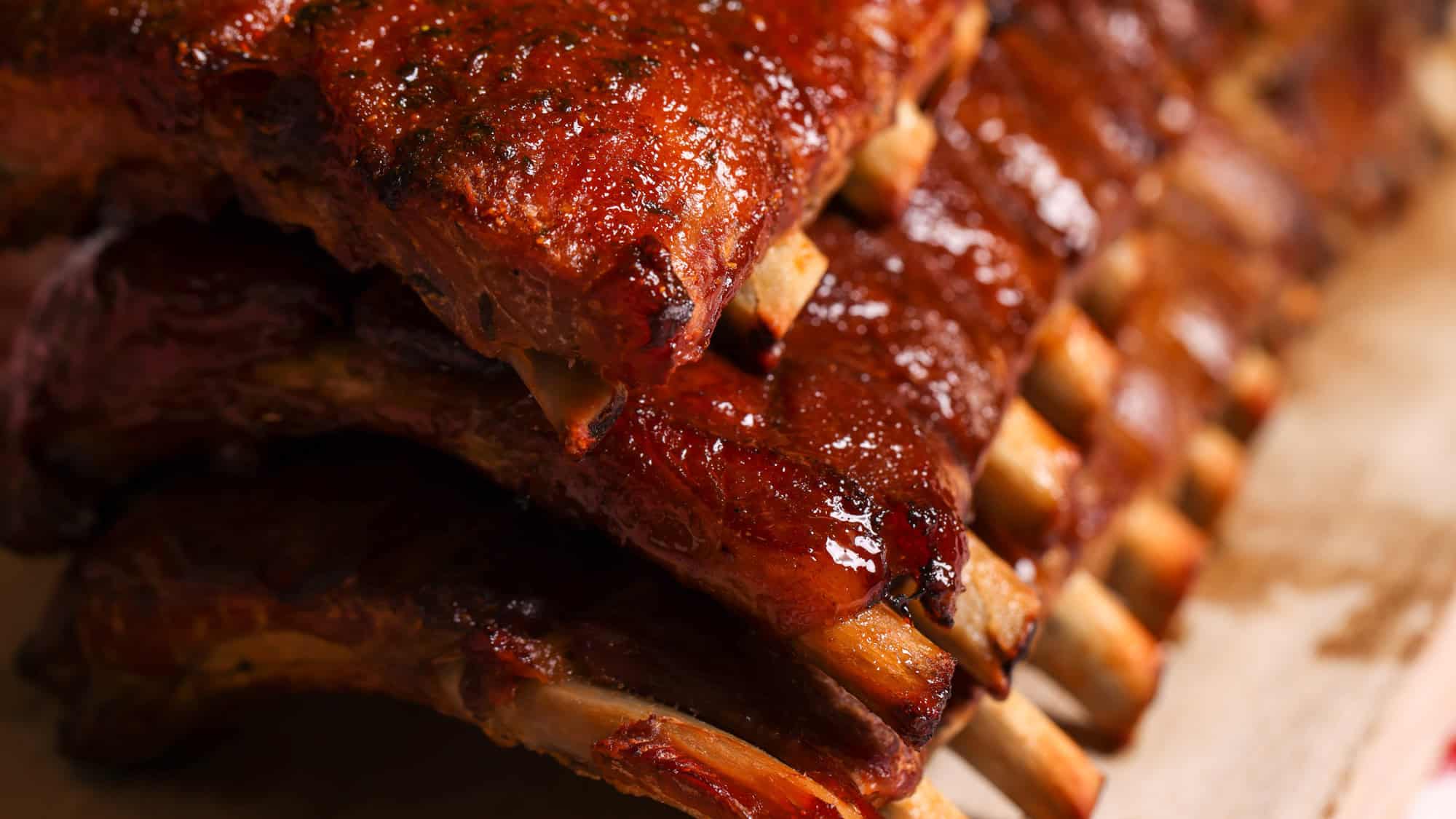 A mouthwatering stack of glazed barbecue ribs is shown in close-up, highlighting the caramelized sauce and tender texture of the meat.