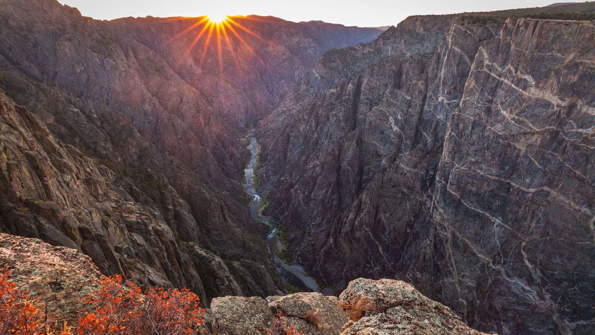 A view for the top of Black Canyon Of Gunnison looking into the canyon with the river running and the sun setting.