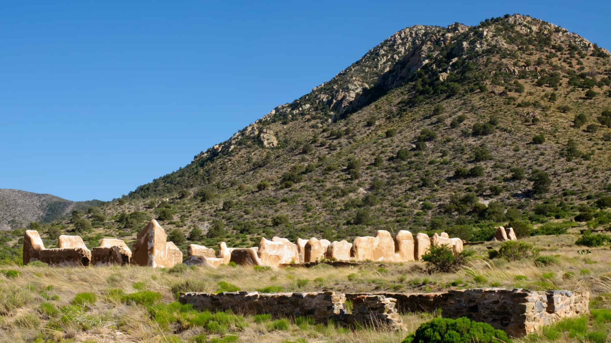 Crumbling adobe walls of the historic Fort Bowie ruins stand against the backdrop of Arizona’s arid, shrub-covered hills and rocky mountains under a clear blue sky.