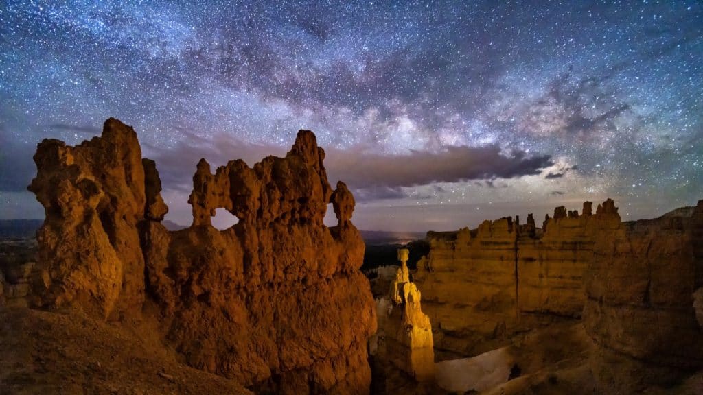 Towering hoodoos and rock formations in Bryce Canyon glow softly under a brilliant, star-studded sky.