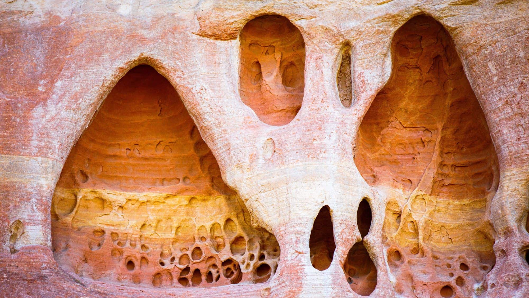 A scenic view of towering red rock formations with layers of sedimentary rock and rugged cliffs. Sparse vegetation and desert terrain surround the formations, creating a dramatic and picturesque landscape.