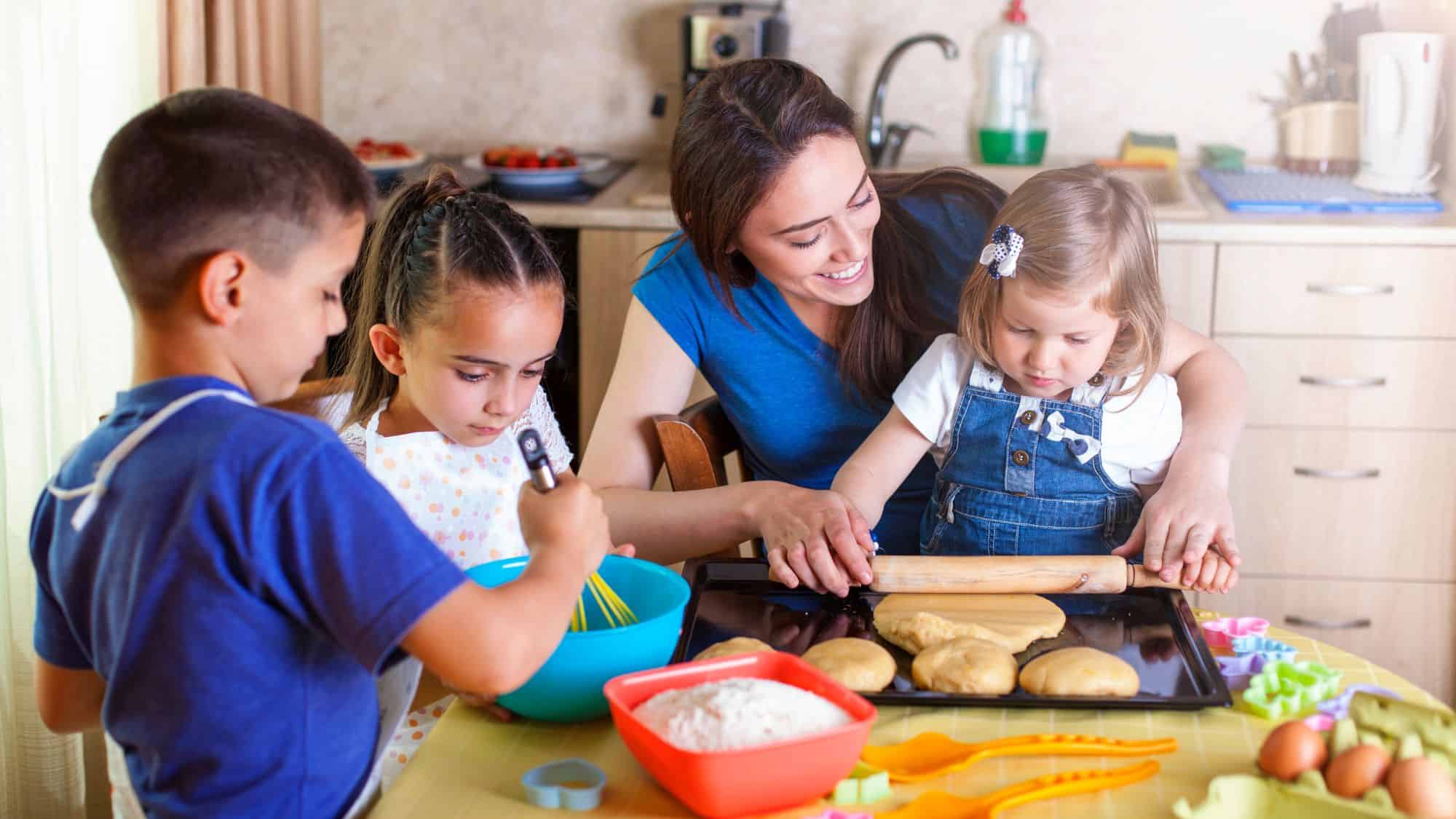 A group of children and an adult engaging in baking activities in a kitchen. The children are mixing ingredients, rolling dough, and preparing cookies, with a warm, family-friendly atmosphere.