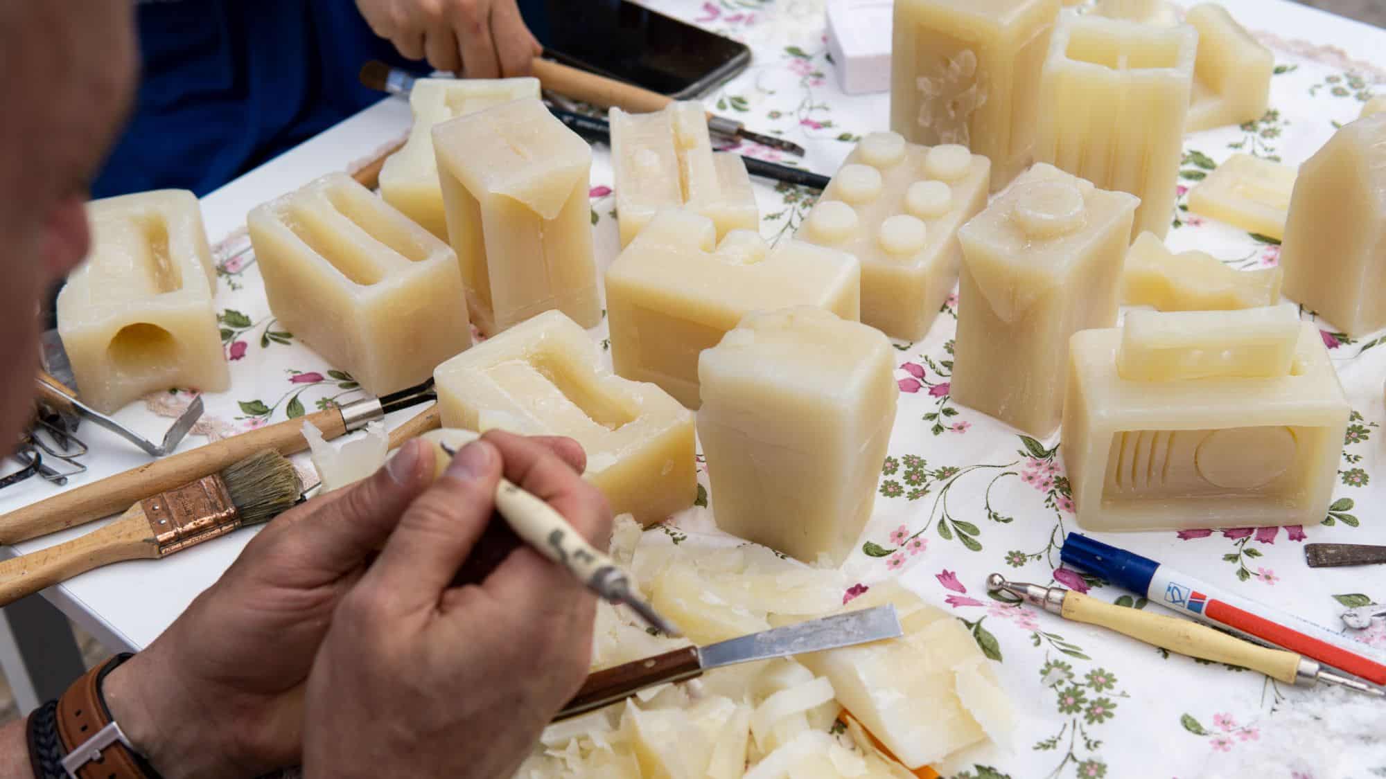 Hands carve intricate shapes out of soap blocks on a work table filled with tools, showcasing a creative soap-making activity.