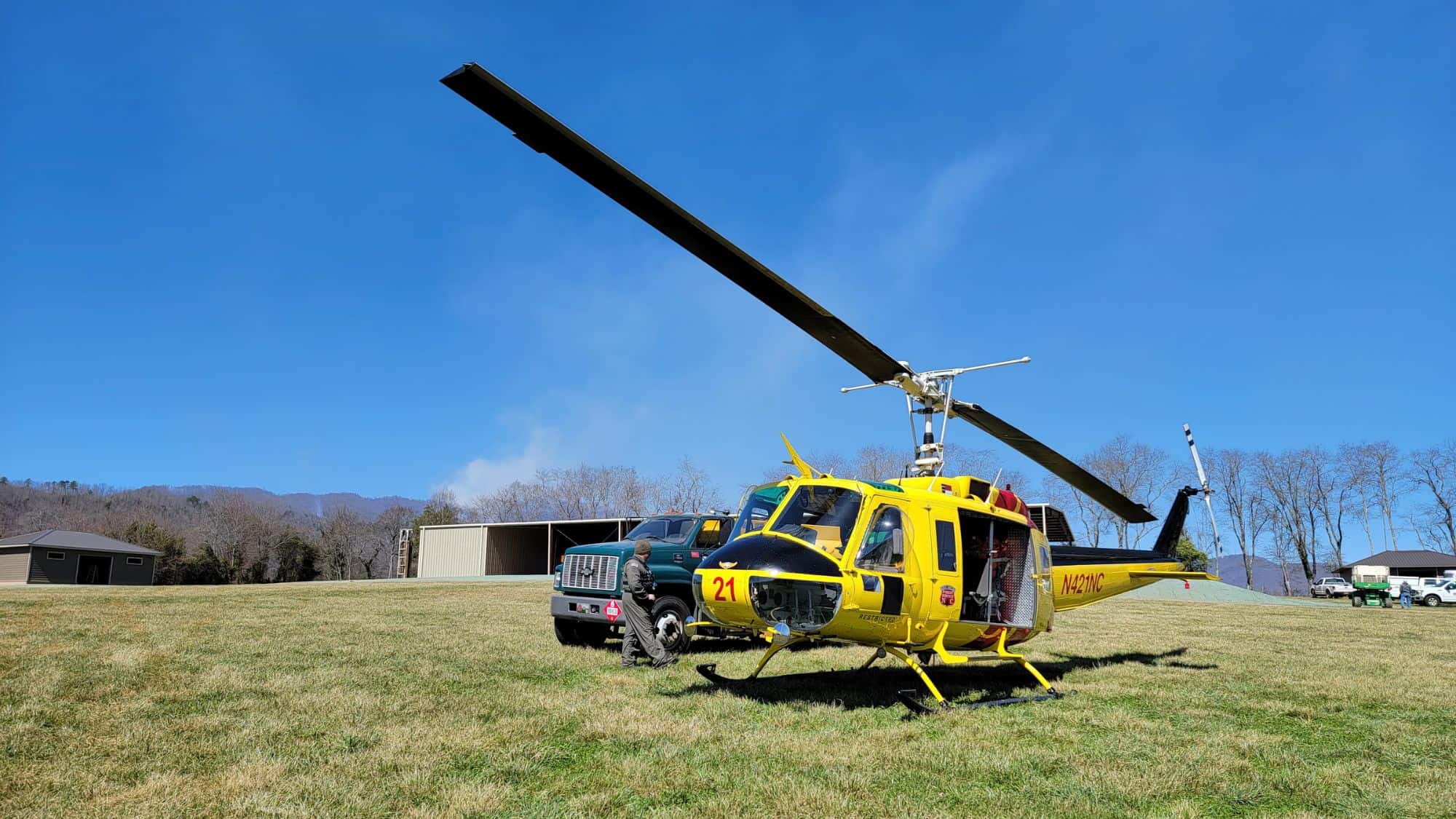 A bright yellow firefighting helicopter sits on a grassy field under a clear sky, prepared for operations related to the Thomas Divide Complex Fire.
