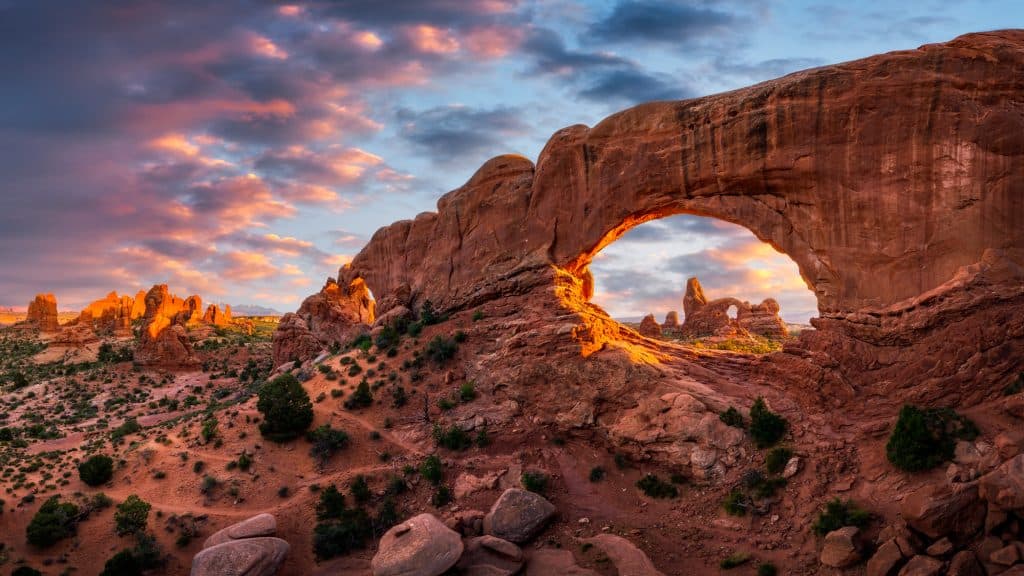 A breathtaking shot of Turret Arch framed through the North Window Arch in Arches National Park, with golden sunlight illuminating the rugged red rock landscape.