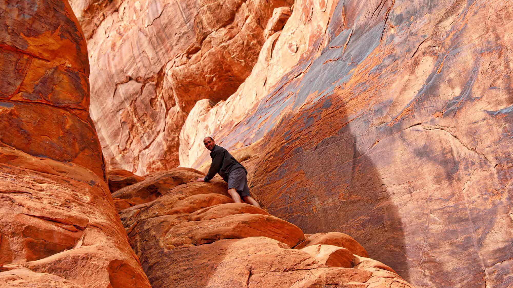A man climbs rugged red sandstone rocks in Arches National Park, showcasing the dramatic textures and hues of the park's distinctive landscape.