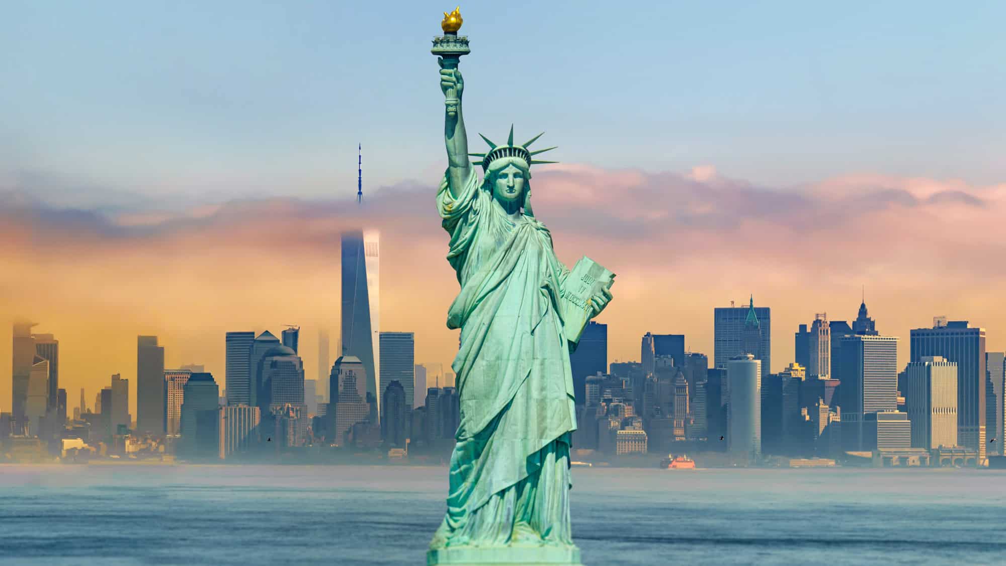The Statue of Liberty holds her torch high in the foreground, with the New York City skyline and a colorful, misty sky in the background, blending iconic symbols of freedom and urban grandeur.
