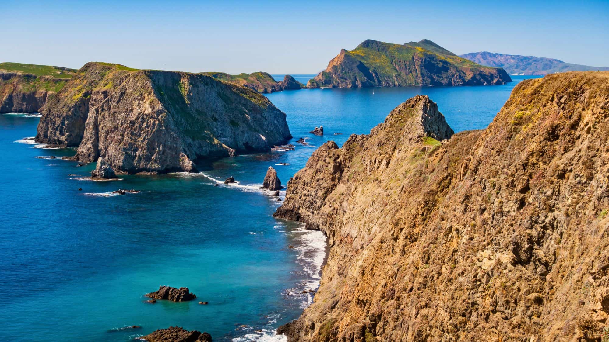 A breathtaking view of the rocky cliffs and deep blue waters of Channel Islands National Park, with small islands stretching into the distance under a clear sky.