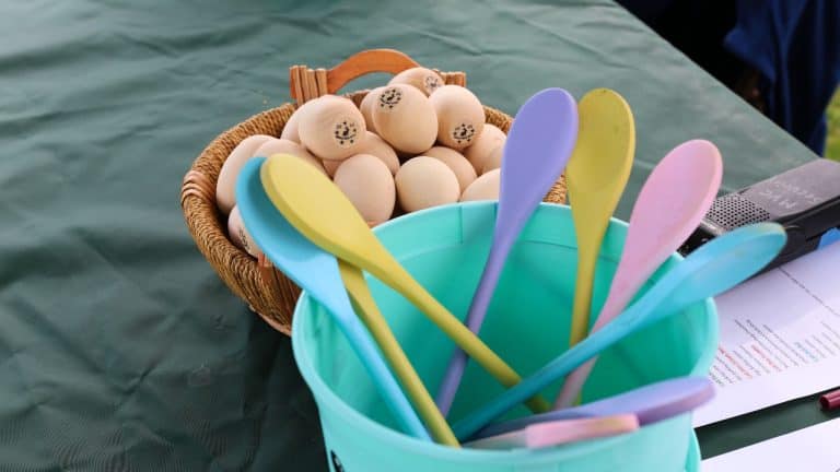 A bucket of painted wooden spoons sits next to a bucket of plain wooden eggs on a table. Wooden spoons and wooden eggs ready for fun at the Easter Egg Roll!