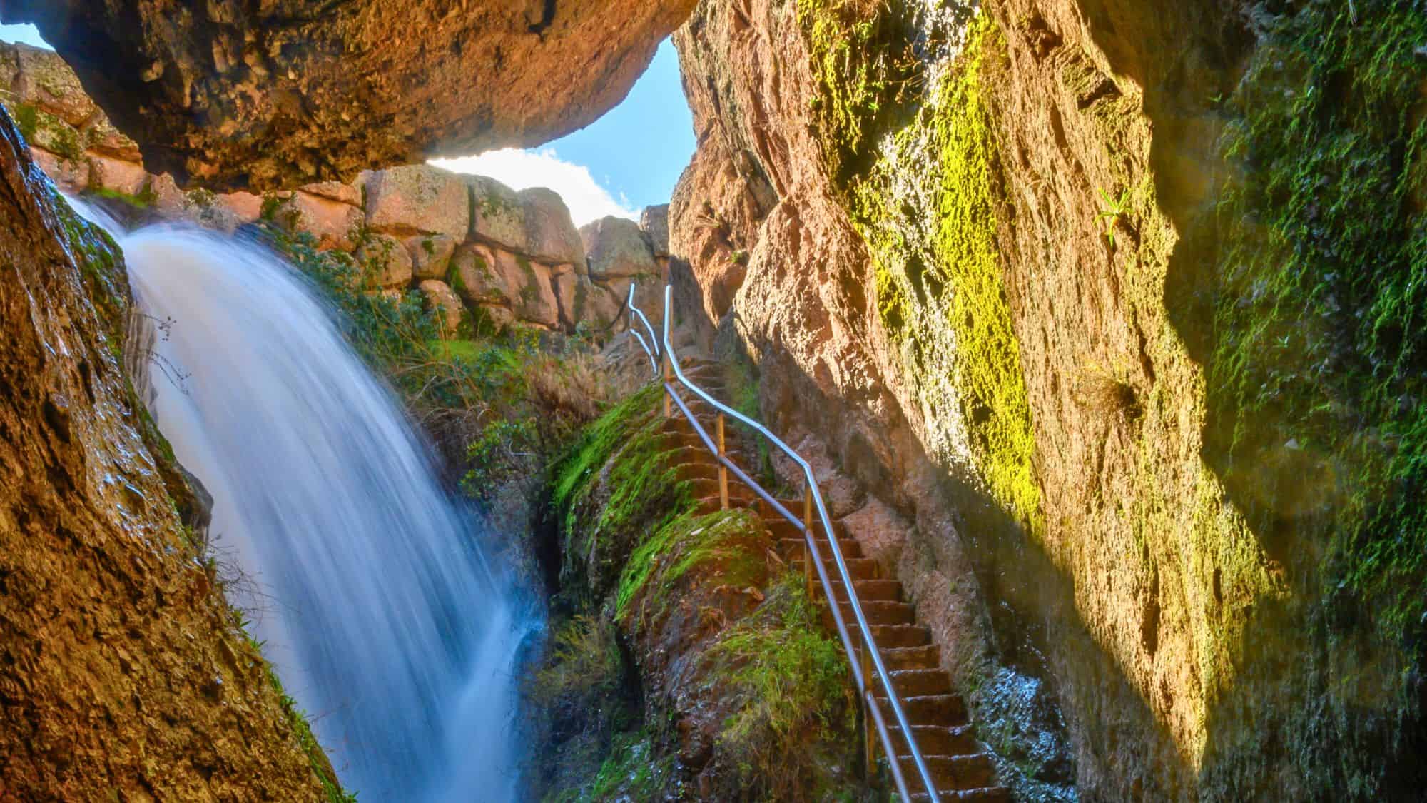 A breathtaking waterfall cascades down the rock face near the Moses Spring Trail, with moss-covered steps leading upward through a narrow canyon.