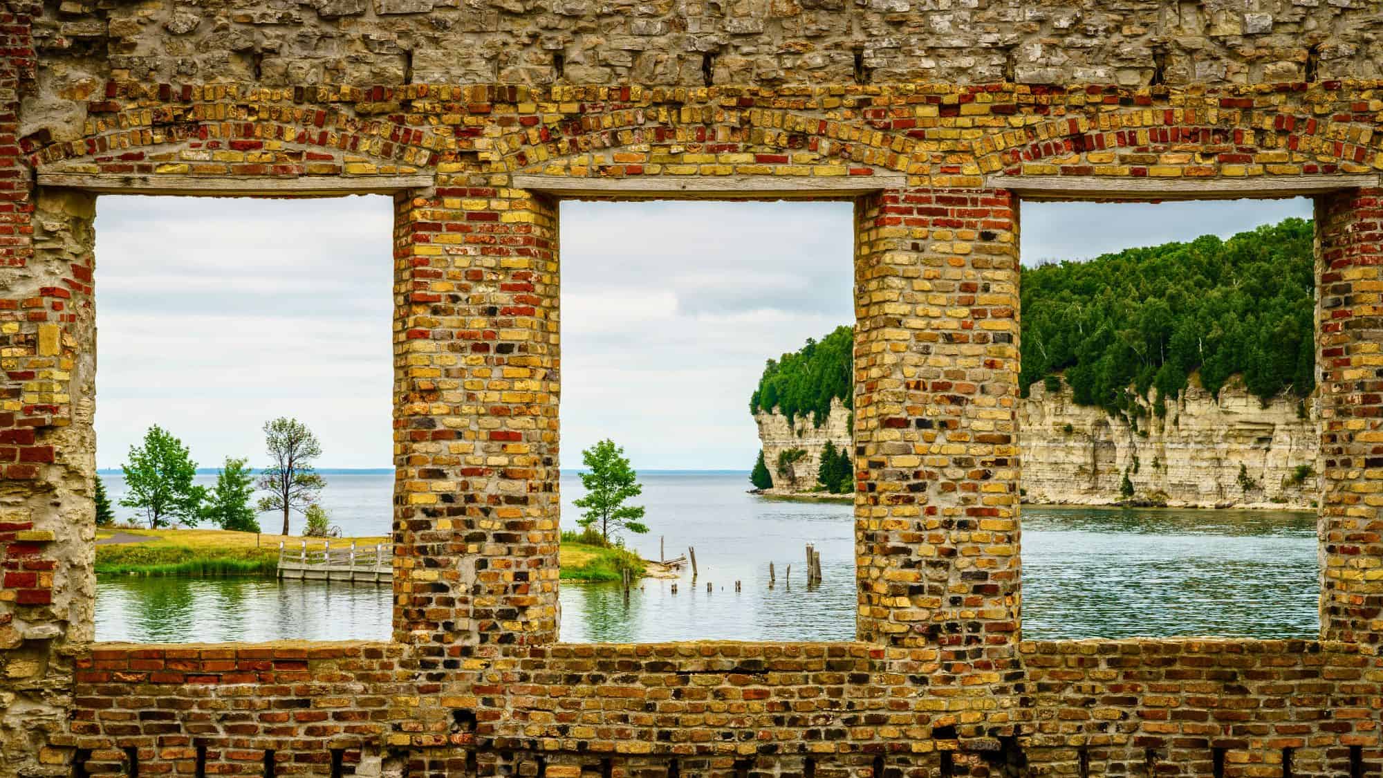 A brick ruin frames a gorgeous view of limestone cliffs and Lake Michigan’s turquoise waters at Fayette Historic State Park, with trees dotting the shoreline beyond.
