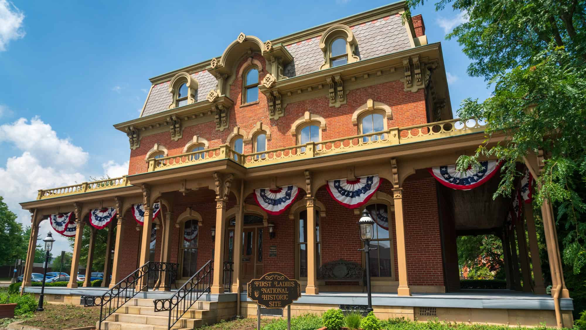 A stately brick Victorian house is adorned with patriotic red, white, and blue bunting. The sign in front reads “First Ladies National Historic Site.”
