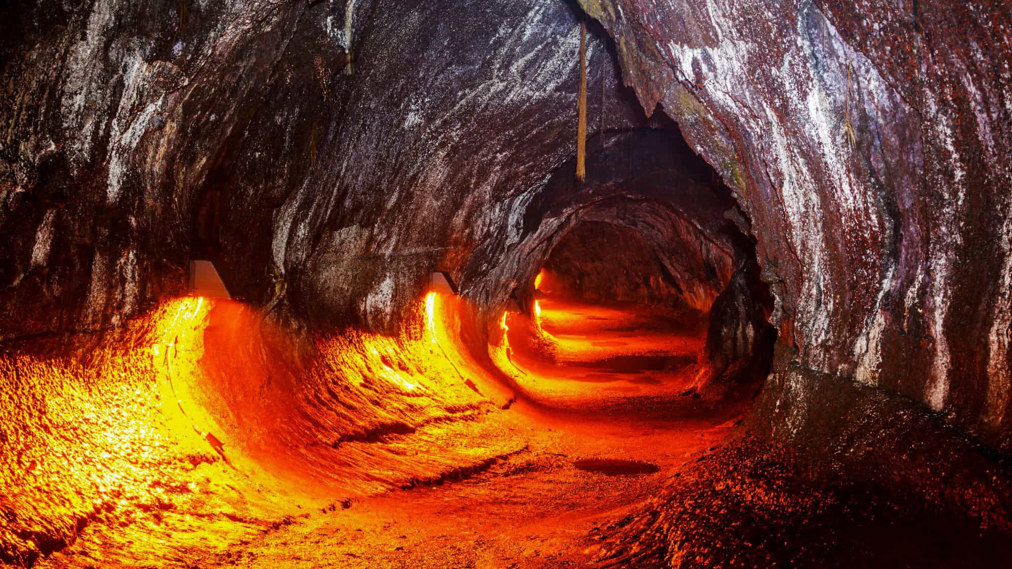 A glowing orange lava tube tunnel with a curved, rocky ceiling and illuminated path creates a dramatic, otherworldly scene.