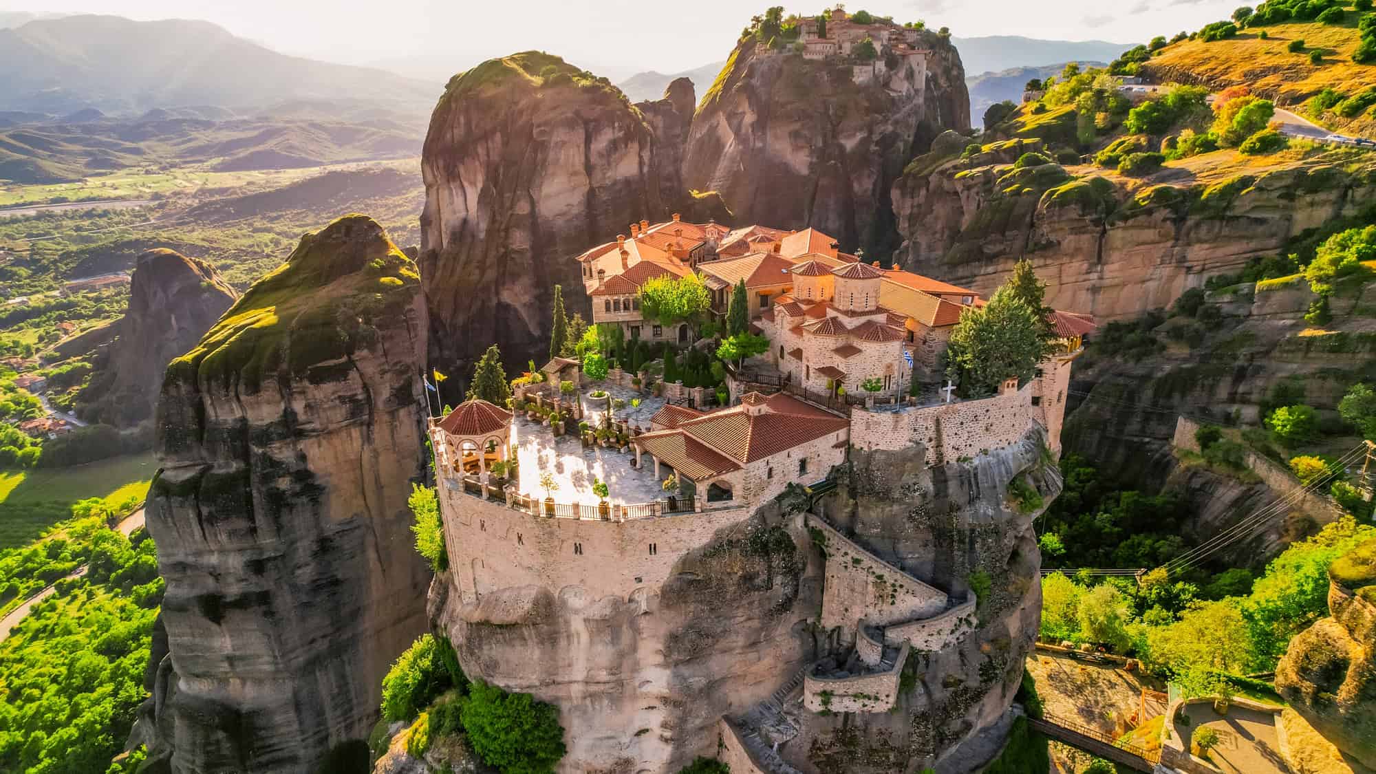 Historic monasteries perched atop giant rock pillars surrounded by a stunning green landscape in Meteora, Greece.