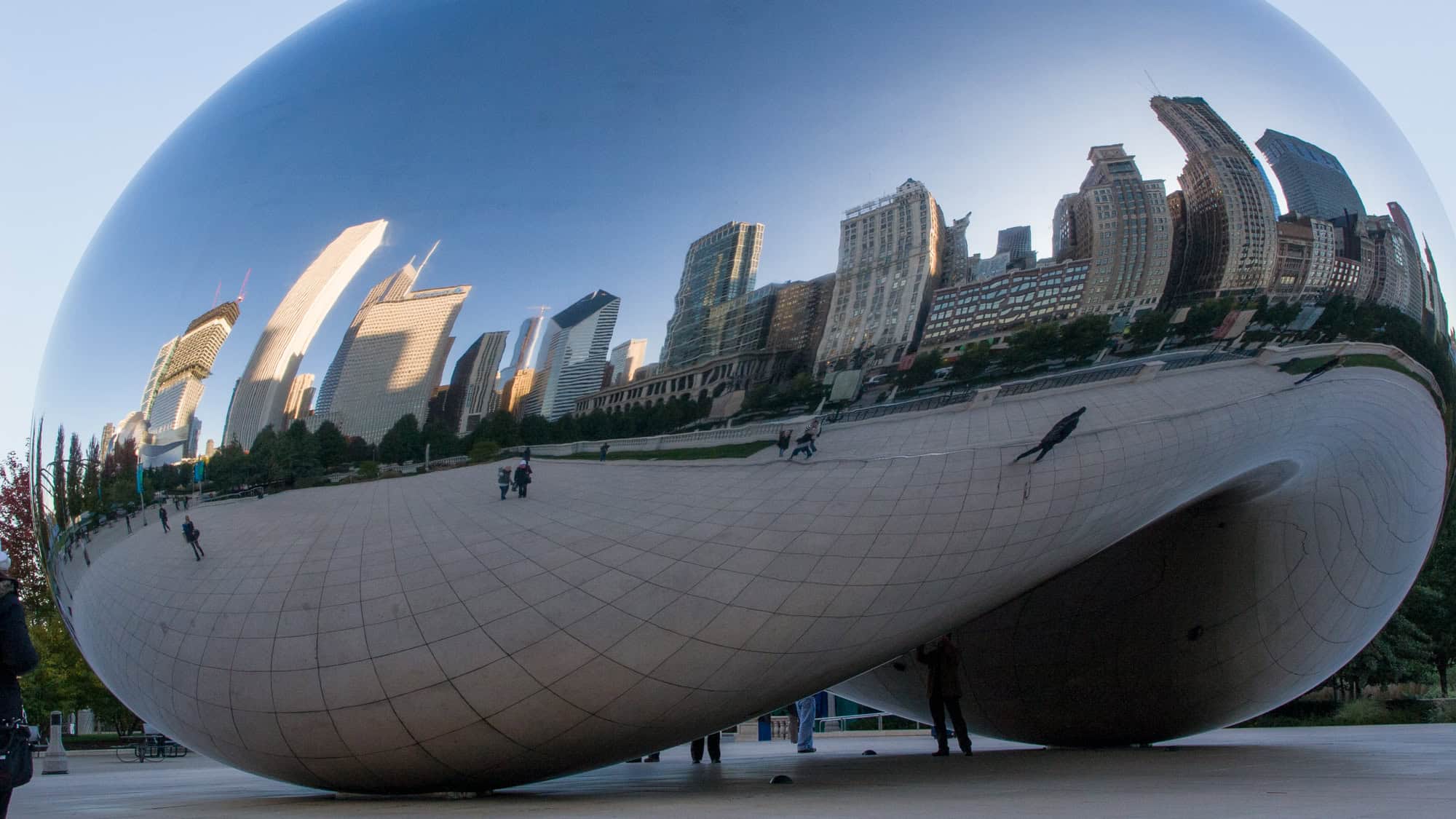 A massive, mirrored sculpture reflects the Chicago skyline in its curved surface, creating a warped cityscape on its stainless steel exterior in Millennium Park.