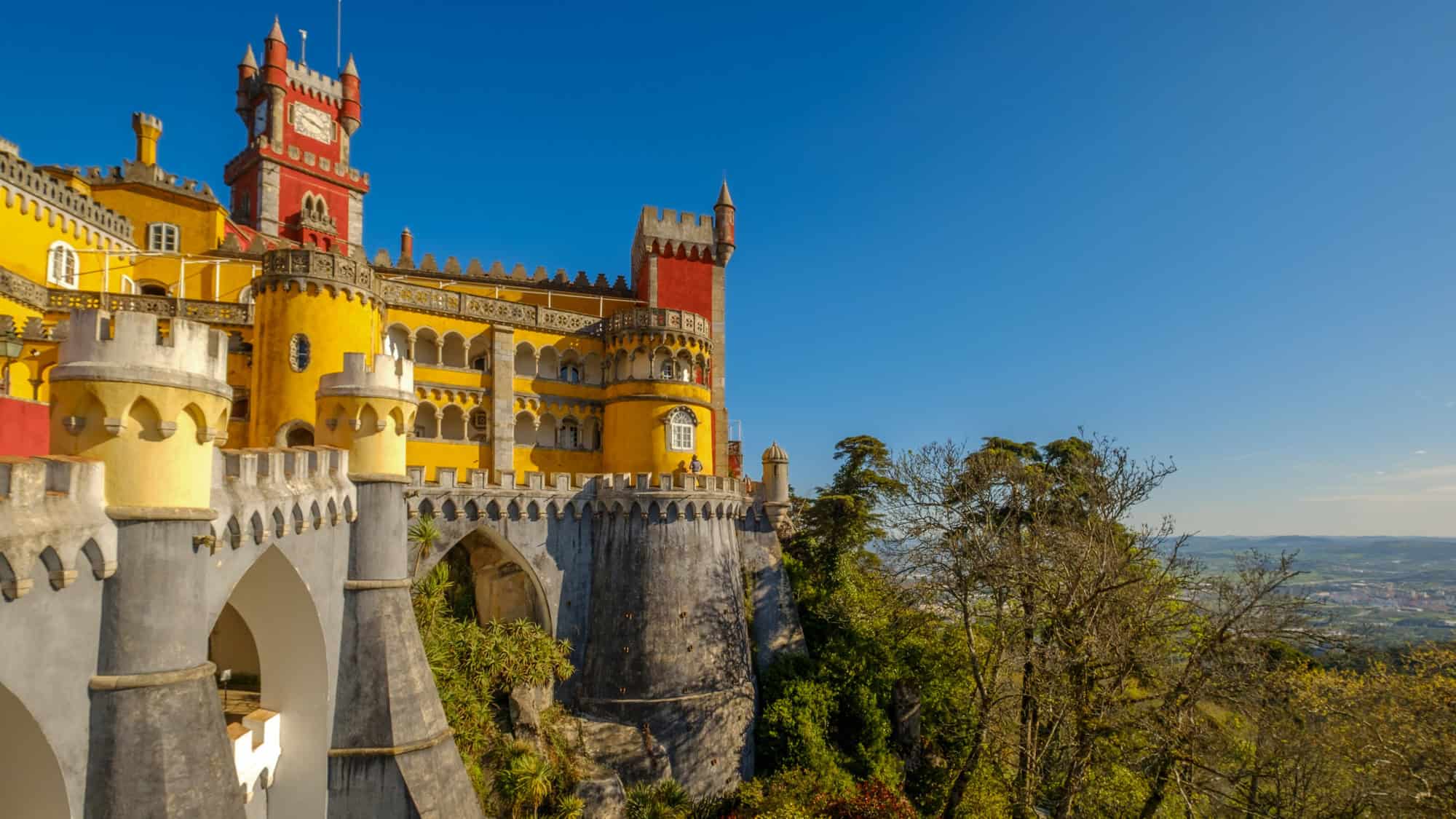 Vibrant yellow and red Pena Palace in Sintra, Portugal, perched on a rocky hilltop under a bright blue sky.