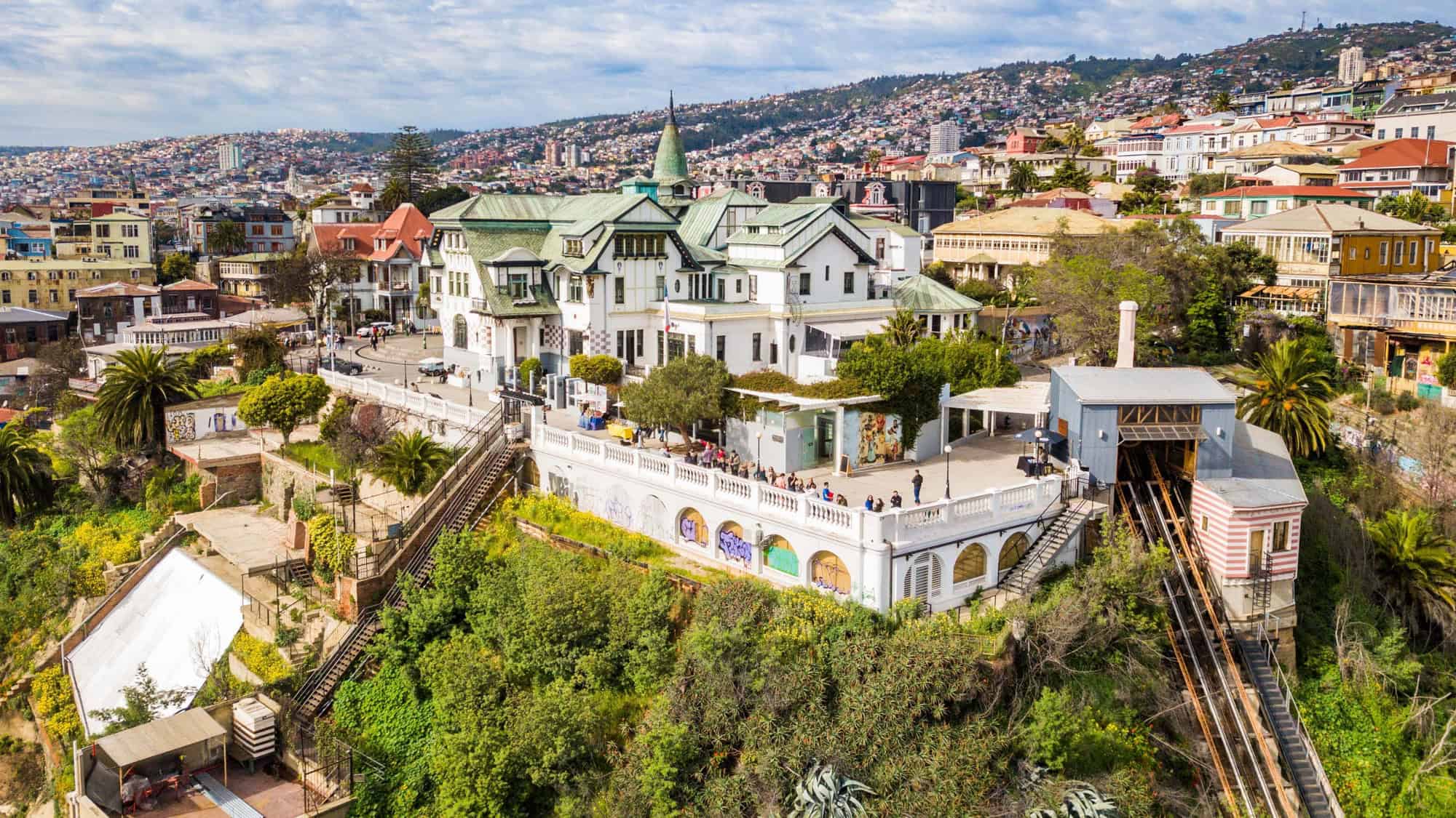 Colorful hillside view of Valparaíso, Chile, featuring funicular tracks, historic houses, and a busy urban sprawl stretching into the distance.