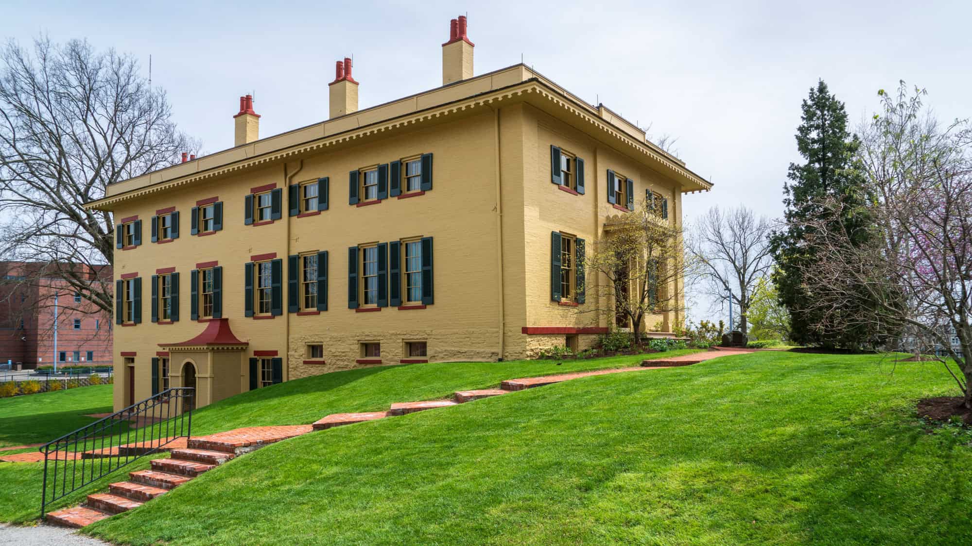A yellow Federal-style building with green shutters and red trim sits on a well-manicured lawn. This was the childhood home of President William Howard Taft.