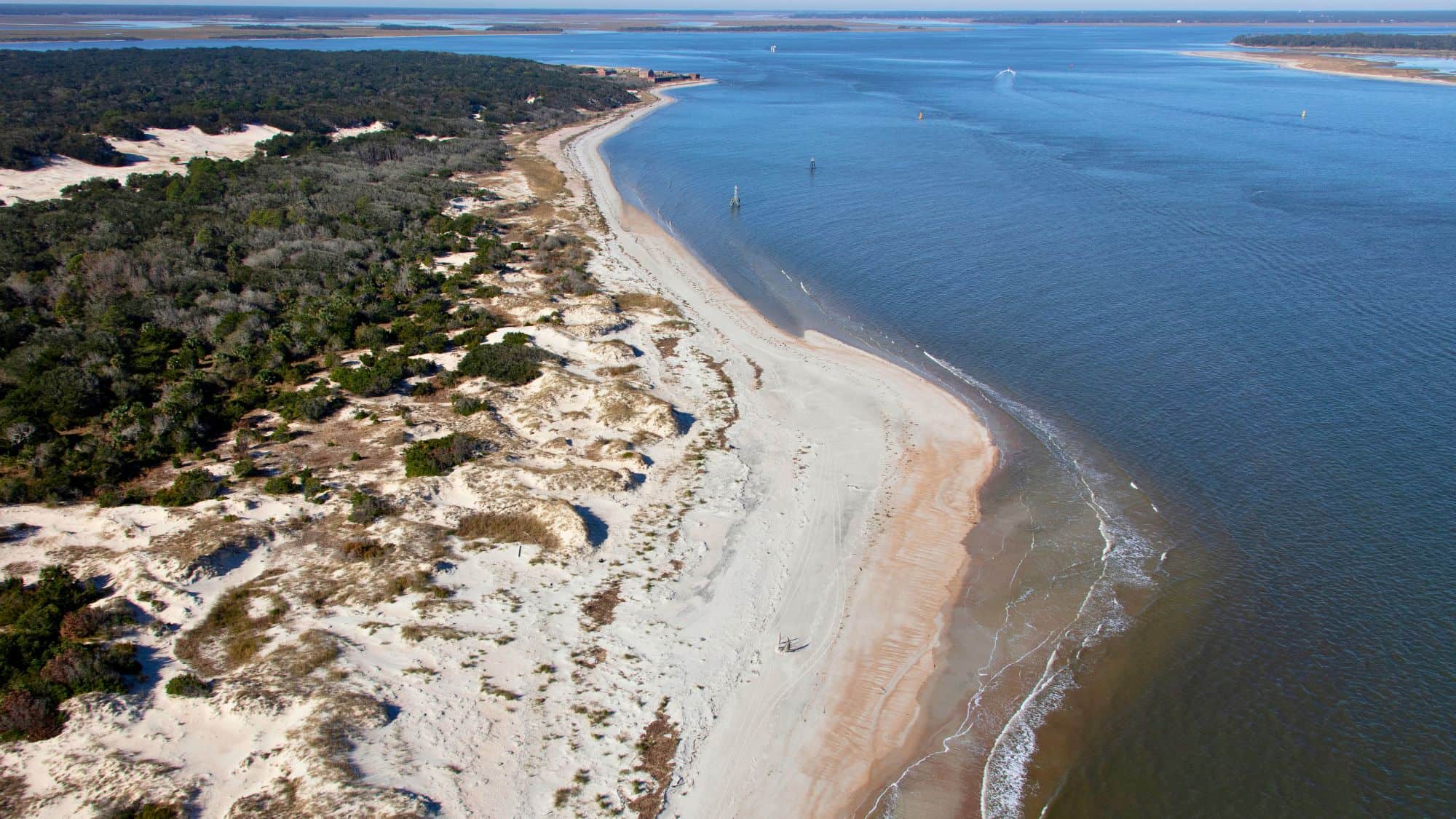 Aerial view of Fort Clinch State Park showcasing a wide sandy beach curving along the shoreline, bordered by dunes and dense greenery with the ocean extending into the horizon.