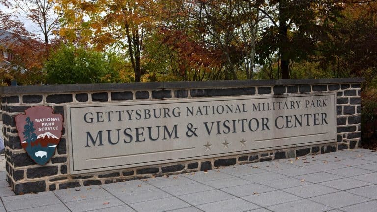 The entrance sign to Gettysburg National Military Park Museum & Visitor Center, featuring the National Park Service emblem and surrounded by autumn foliage.
