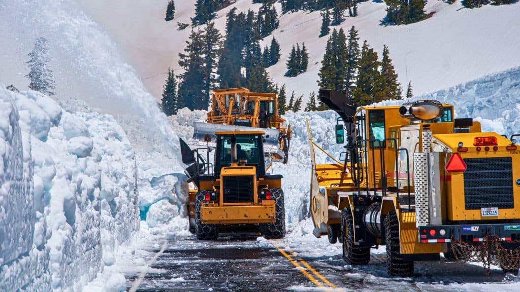 LASSEN, US - Jun 21, 2011: A line of snowplows traversing a street lined with trees on both sides, against a backdrop of snowy terrain
