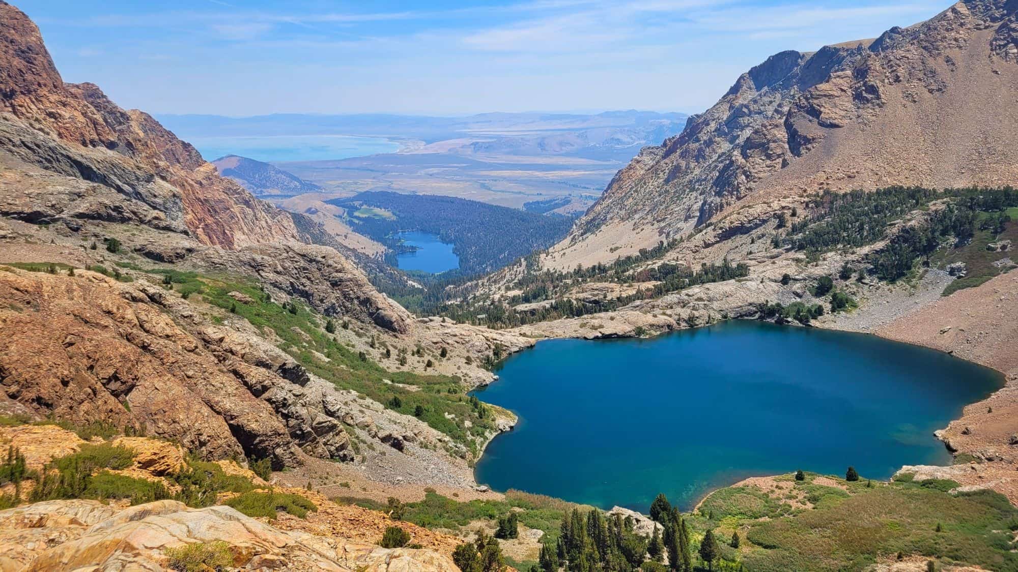 Looking down from Mono Pass, the photo reveals multiple alpine lakes tucked among rocky ridges, with Mono Lake faintly visible in the hazy distance.