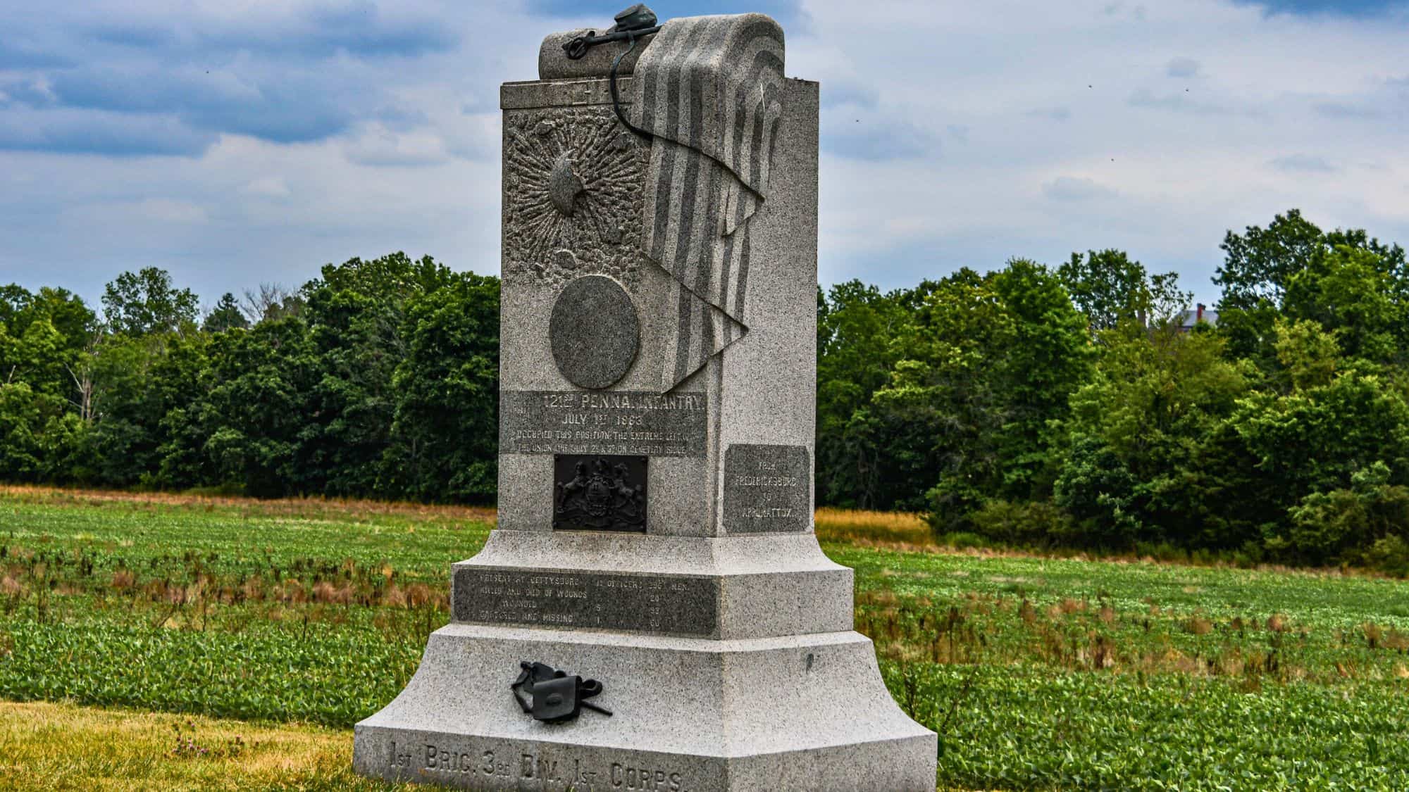 A tall granite monument to the 121st Pennsylvania Infantry stands beside a field with detailed carvings of the American flag and battle emblems.