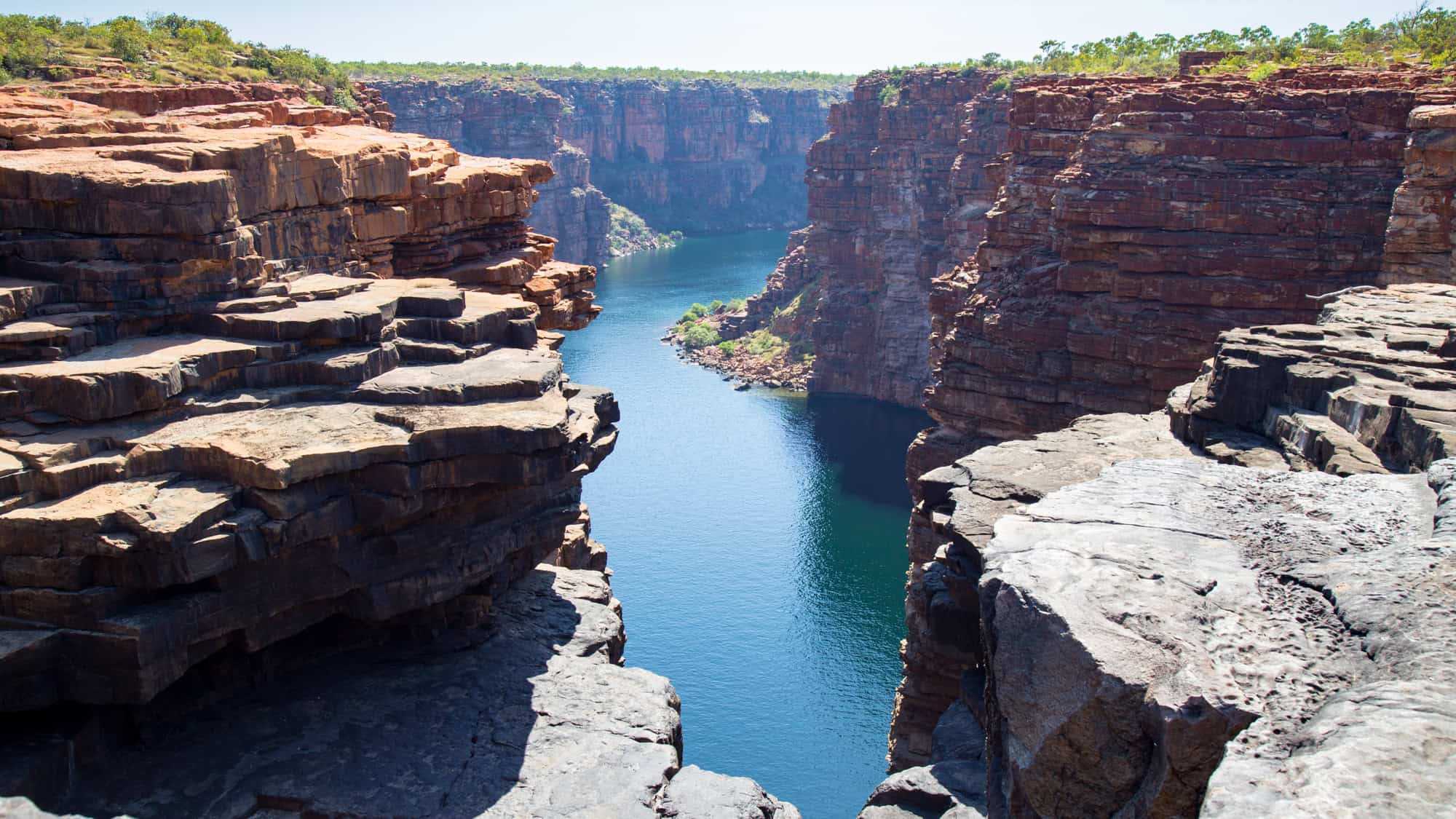 Dramatic red rock cliffs frame the King George River gorge in Kimberley, Australia, with deep blue water running between the vertical canyon walls.
