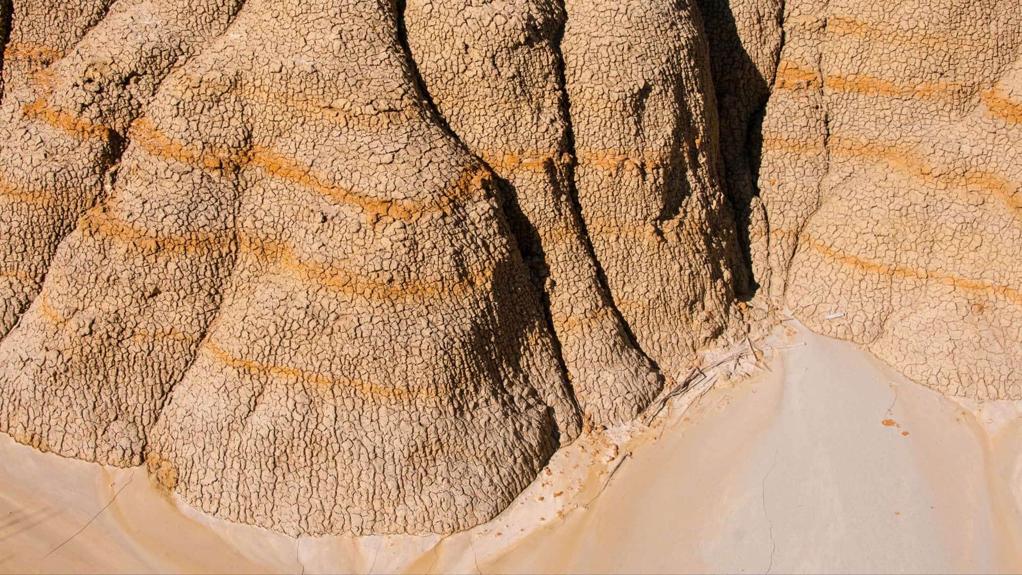 A close-up of dry, cracked buttes featuring distinct horizontal bands of orange and beige, highlighting the erosion patterns in the arid badlands.