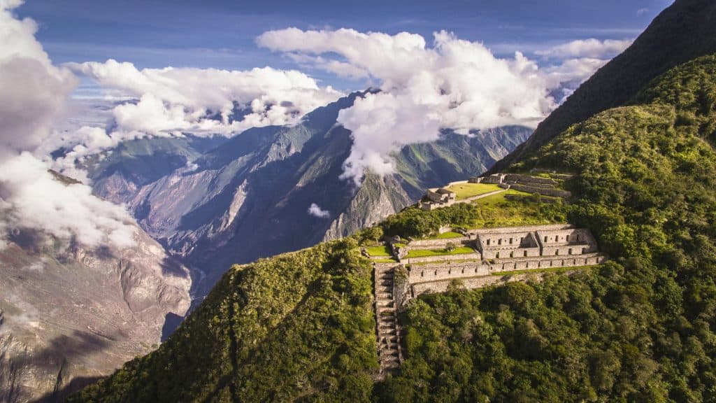 Terraced Incan ruins cling to the edge of a misty mountain in Peru, surrounded by dramatic Andean peaks and drifting clouds, showcasing the remote grandeur of Choquequirao.