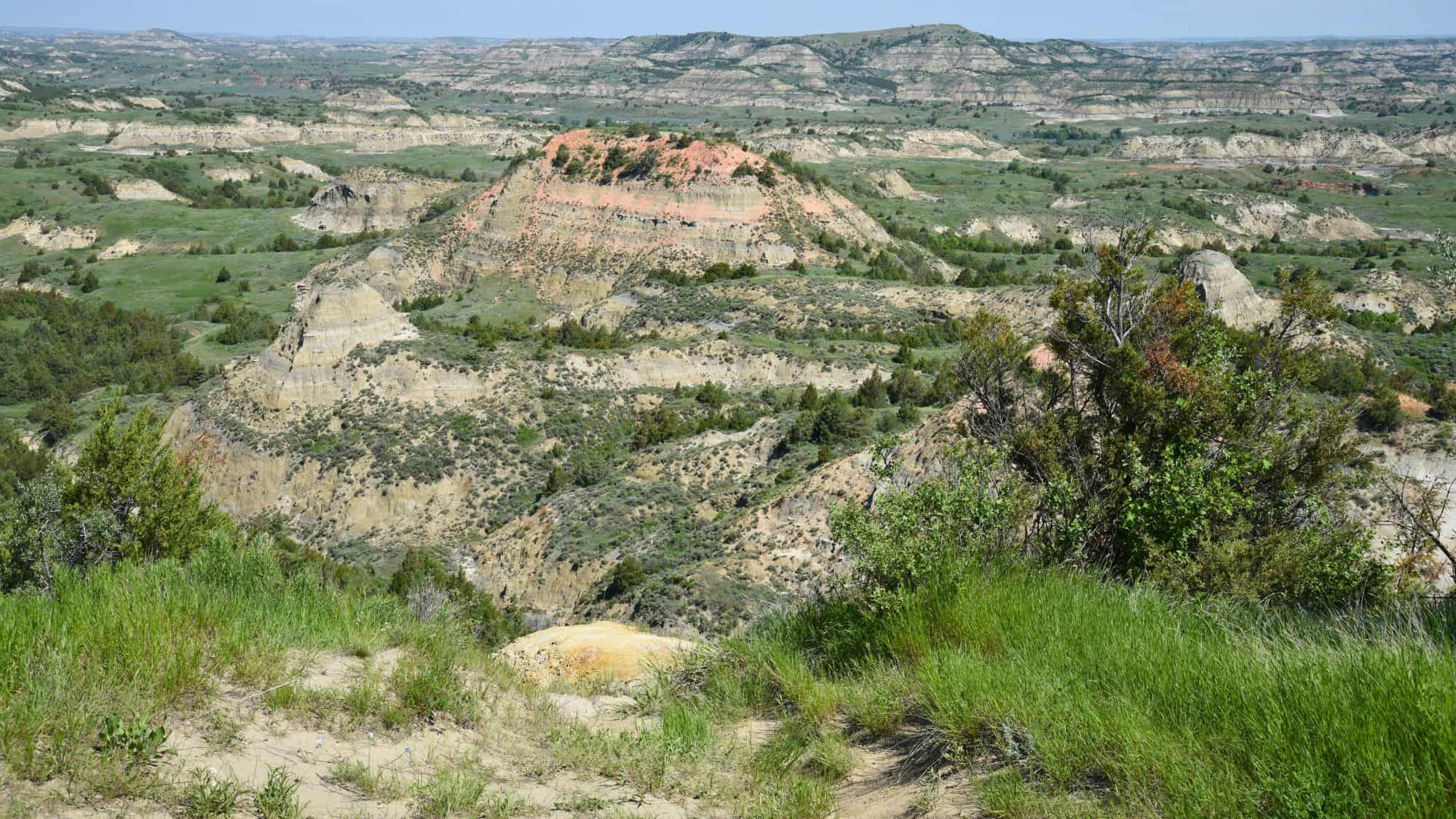 A rugged badlands landscape with layered rock formations in muted browns and tans, spread out under a hazy sky, showcasing North Dakota’s iconic terrain.