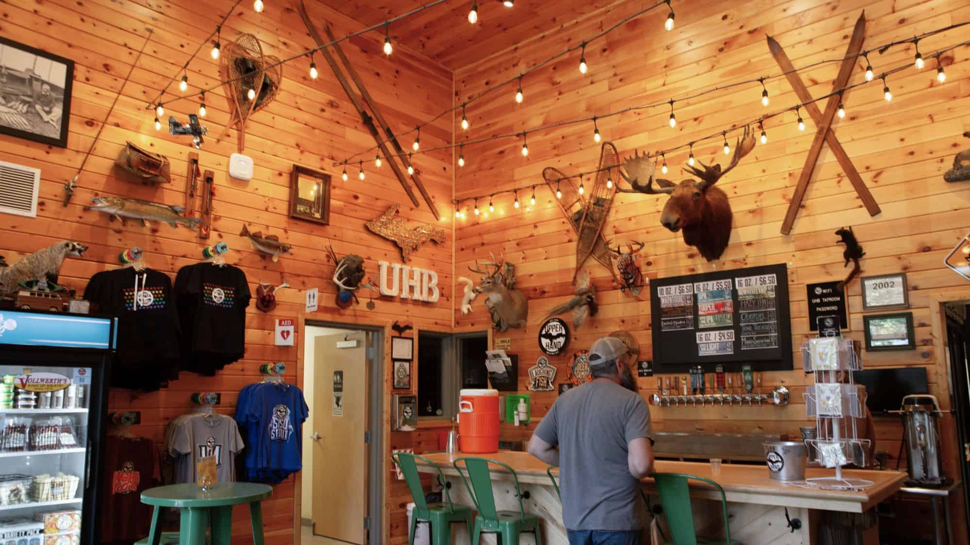 Wood-paneled taproom filled with taxidermy, vintage skis, string lights, and colorful merchandise, creating a lodge-like feel at Upper Hand Brewery.