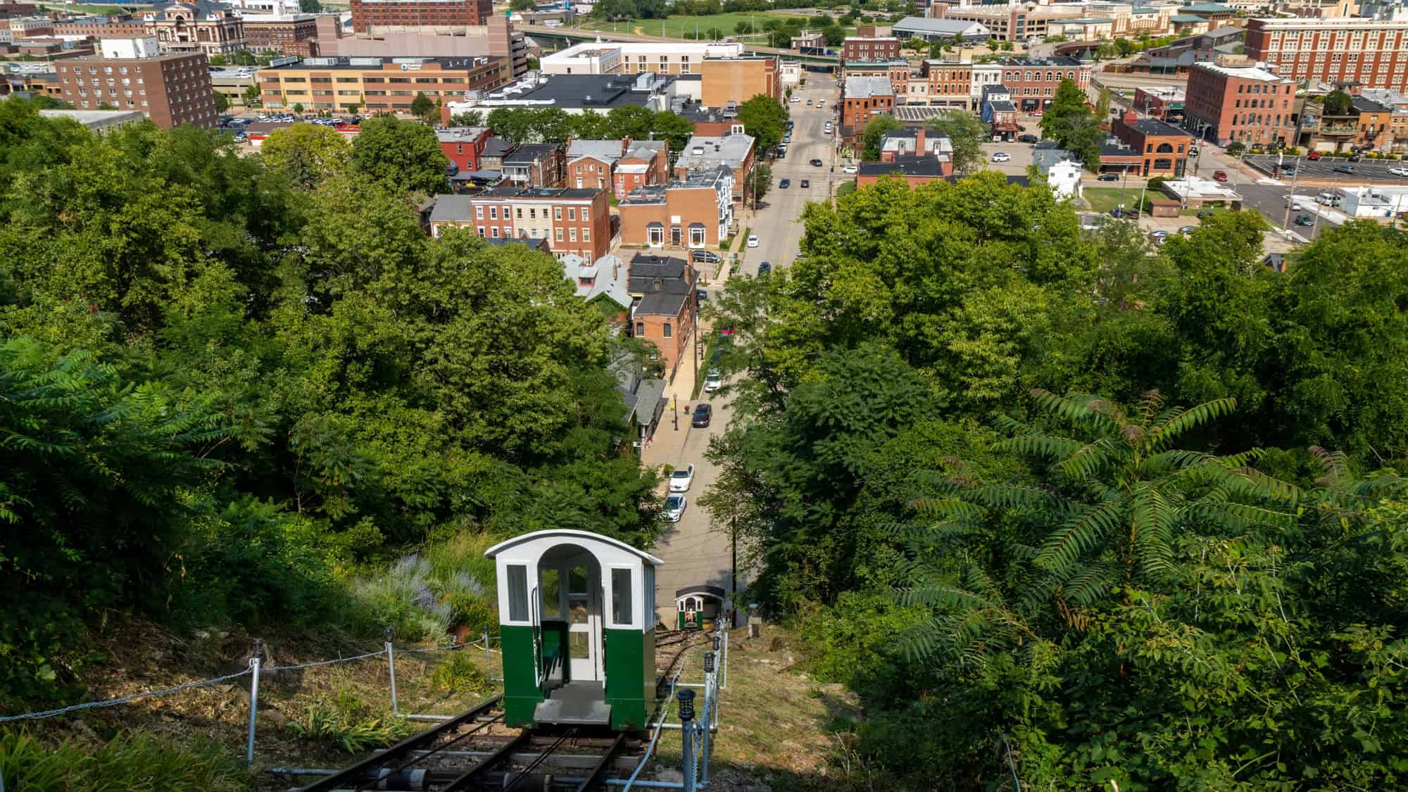A funicular car descends a steep hillside toward downtown Dubuque, Iowa, offering a sweeping view of red brick buildings, residential streets, and the cityscape beyond.