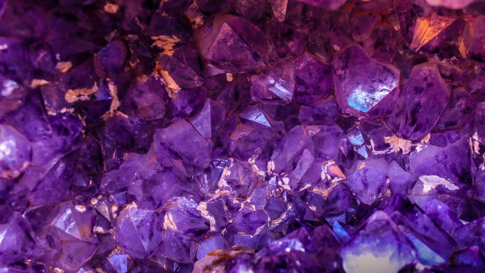 Macro view of jagged, shimmering purple amethyst crystals clustered together, with streaks of white and hints of orange mineral deposits.