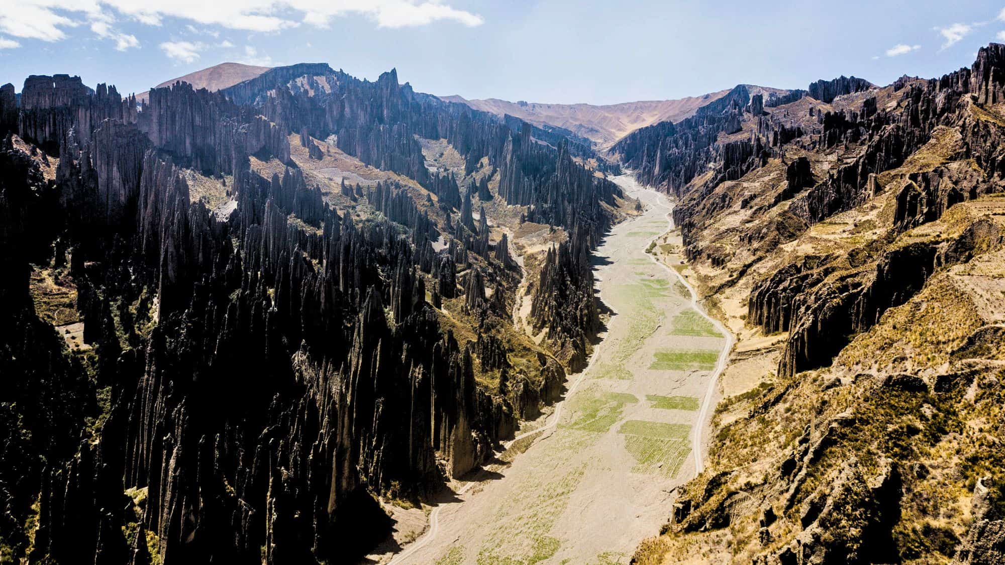 Tall, needle-like rock spires tower over a narrow, dry valley with scattered green patches in Bolivia’s otherworldly Valle de las Ánimas.