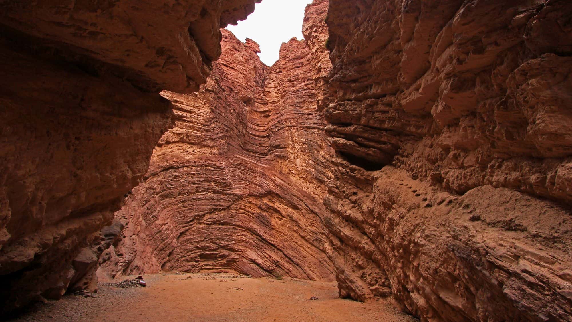 Massive red sandstone walls rise dramatically on both sides of a narrow canyon floor in this naturally sculpted formation in northwest Argentina.