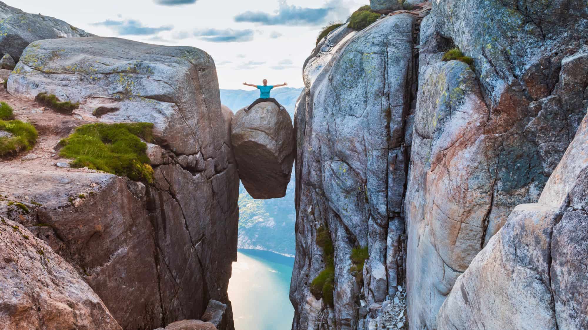 A hiker stands triumphantly atop the famous boulder wedged between cliffs high above a fjord.