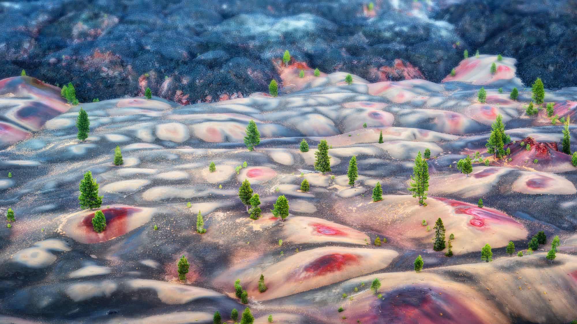 Vibrant volcanic hills in shades of red, orange, and gray are dotted with green conifer trees.