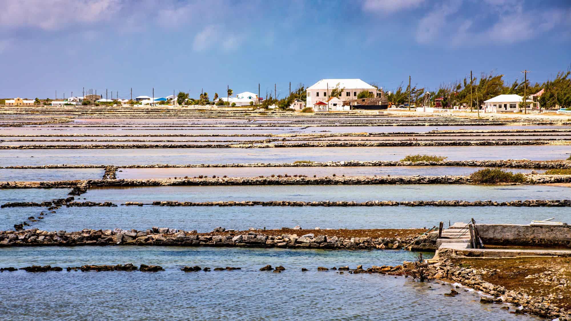 Rows of salt pans stretch across the landscape, with stone dividers and small houses visible in the distance.