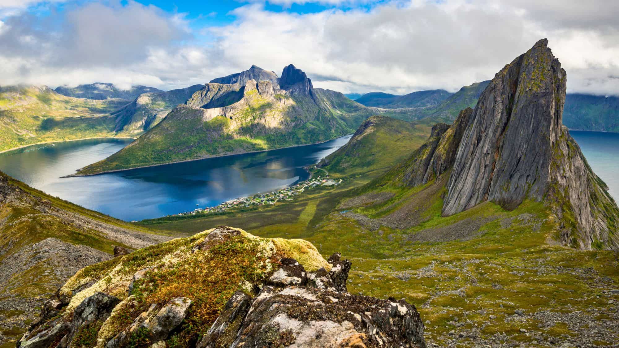 Sharp peaks and deep blue fjords stretch out under a mix of clouds and sun in this rugged mountain scene.