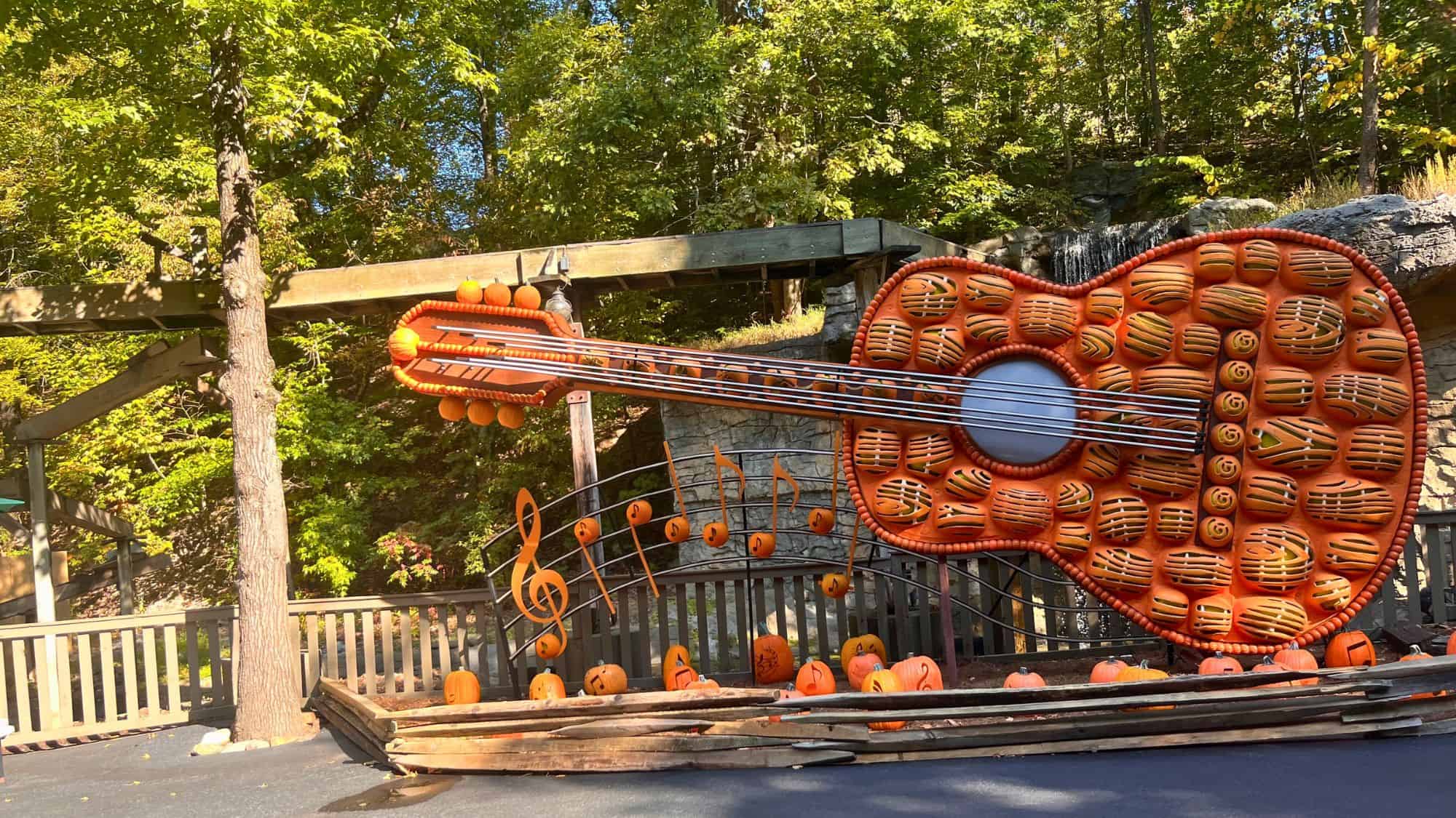 A giant guitar sculpture made entirely of carved orange pumpkins is surrounded by musical note decorations and more pumpkins at its base.