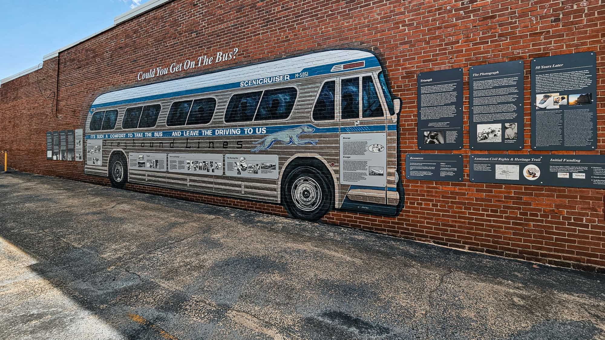 A mural of a Greyhound bus on a brick wall displays civil rights history with educational panels alongside it.